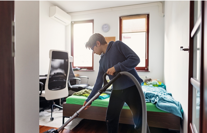 college freshman vacuuming his dorm room floor